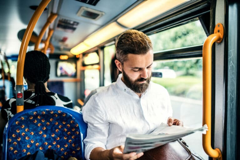 Hipster man sitting on a bus in the city, travelling to work and reading newspapers.